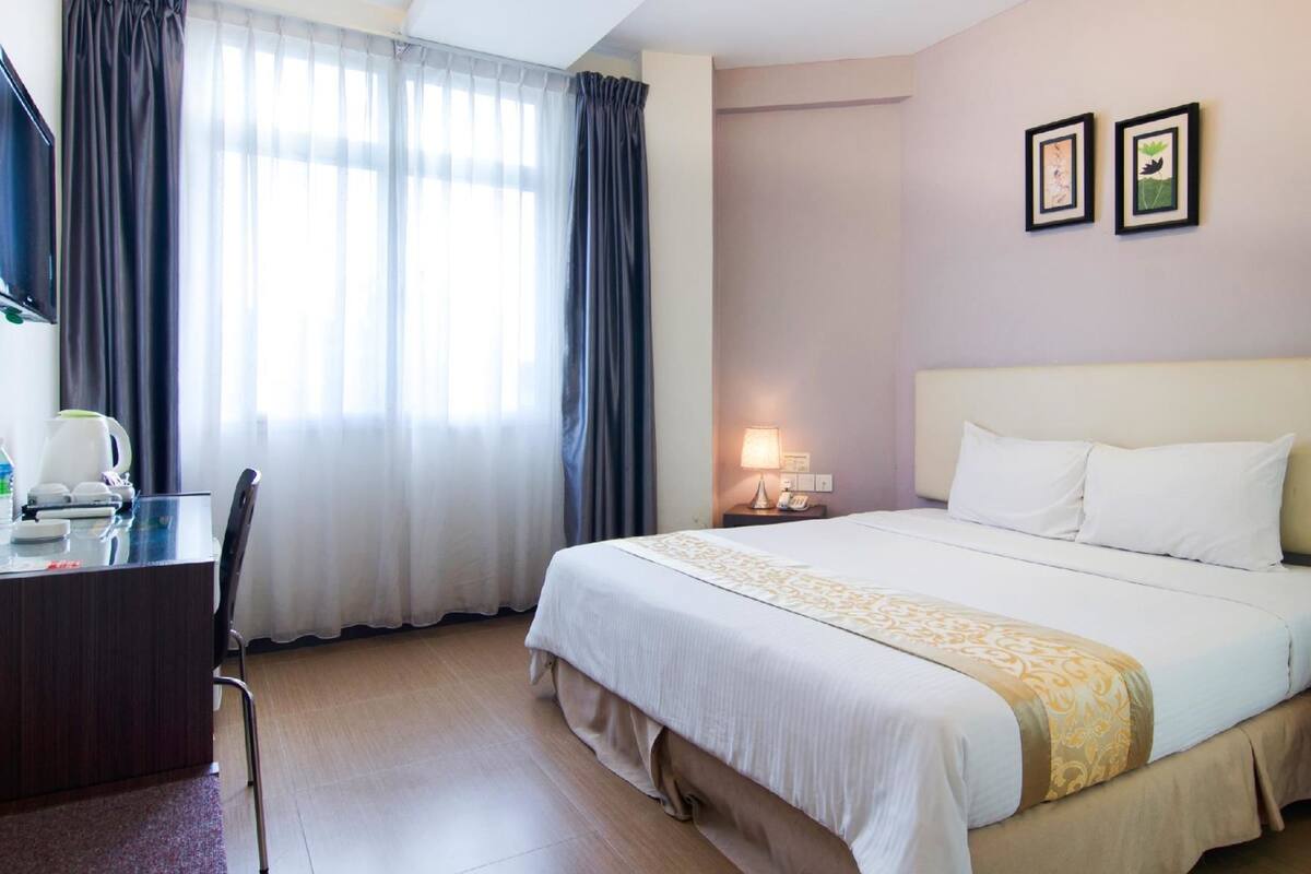 A hotel room with a bed, a desk with a chair, a coffee maker, and curtains.