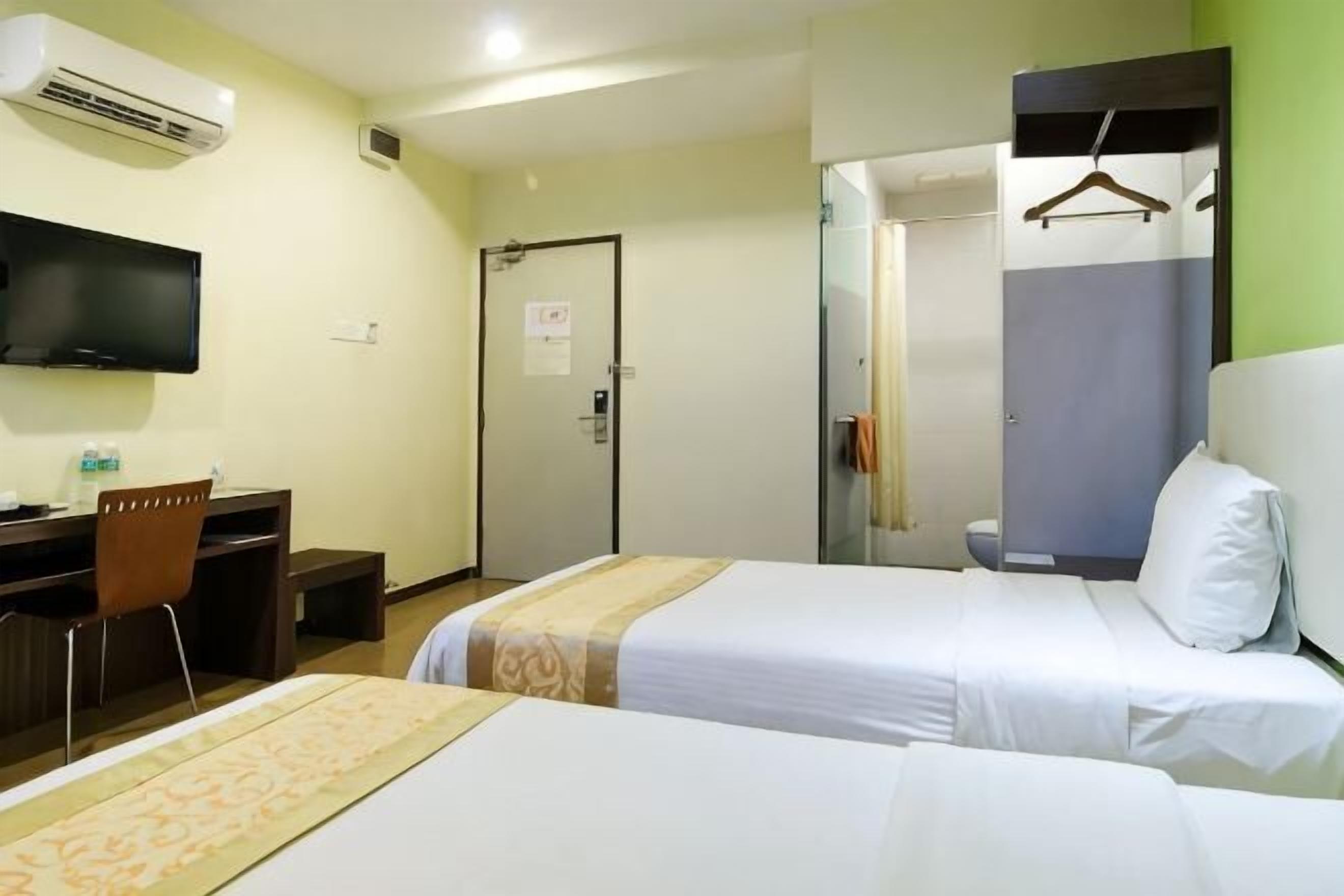 A hotel room with two beds, a desk, a chair, a TV, and a shower area.
