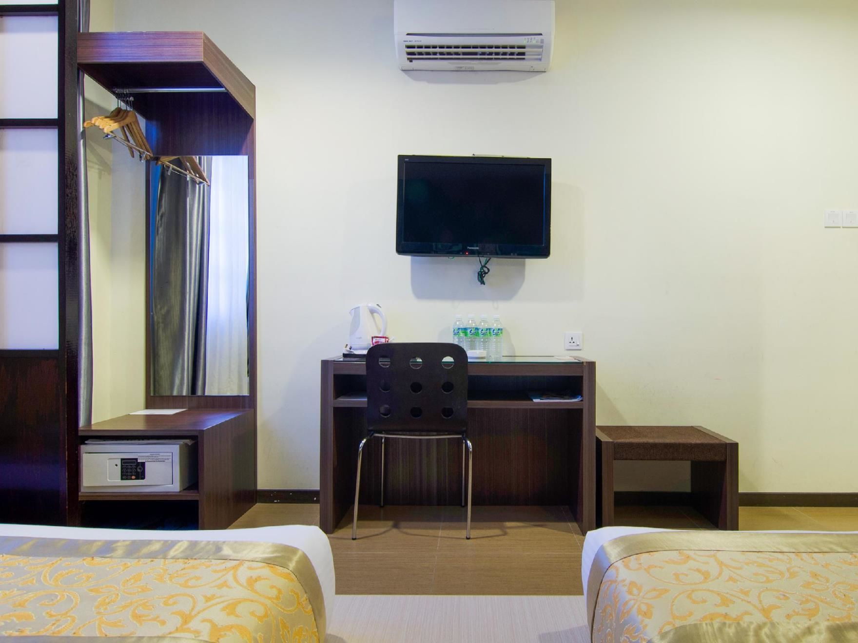 A hotel room with two beds, a desk with a chair, a television, an air conditioning unit, and a mirror.