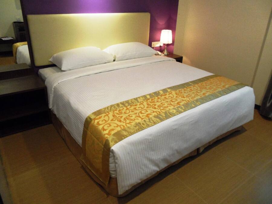 A hotel room with a bed, a nightstand, a lamp, and a mirror.