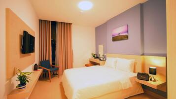 Habitación de hotel con cama, escritorio, silla, televisor, lámpara y un cuadro en la pared.