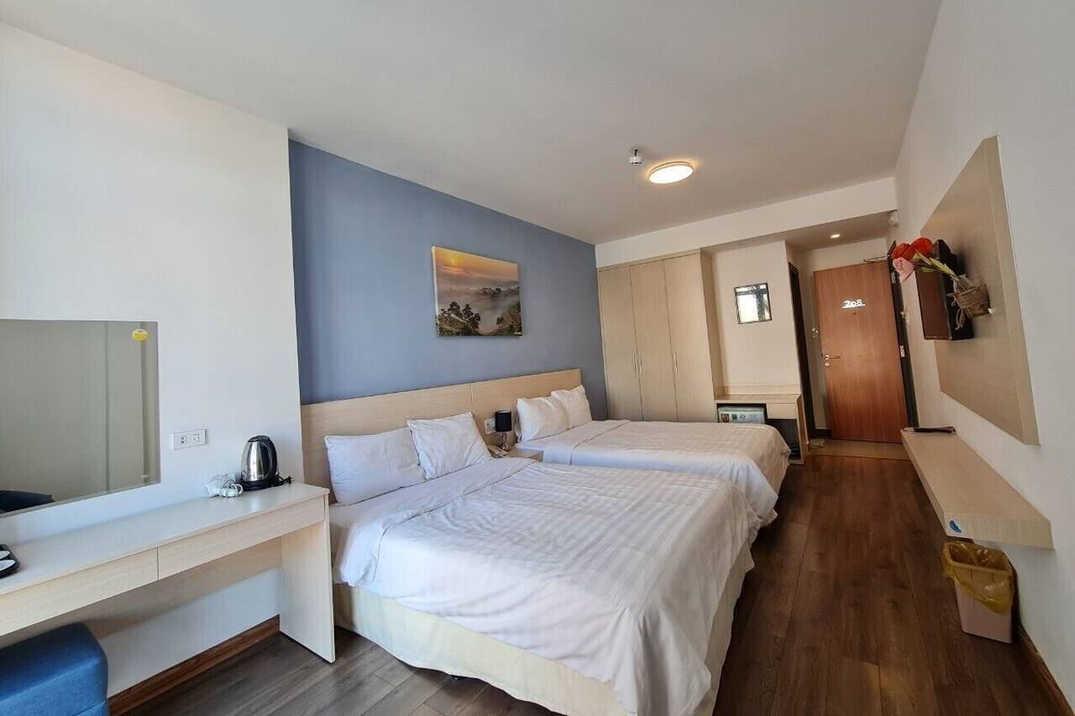 Ein Hotelzimmer mit zwei Betten, einem Schreibtisch, einem Spiegel, einem Gemälde und Holzboden.