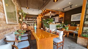 Un café acogedor con mobiliario de madera, una barra central y diversas plantas.
