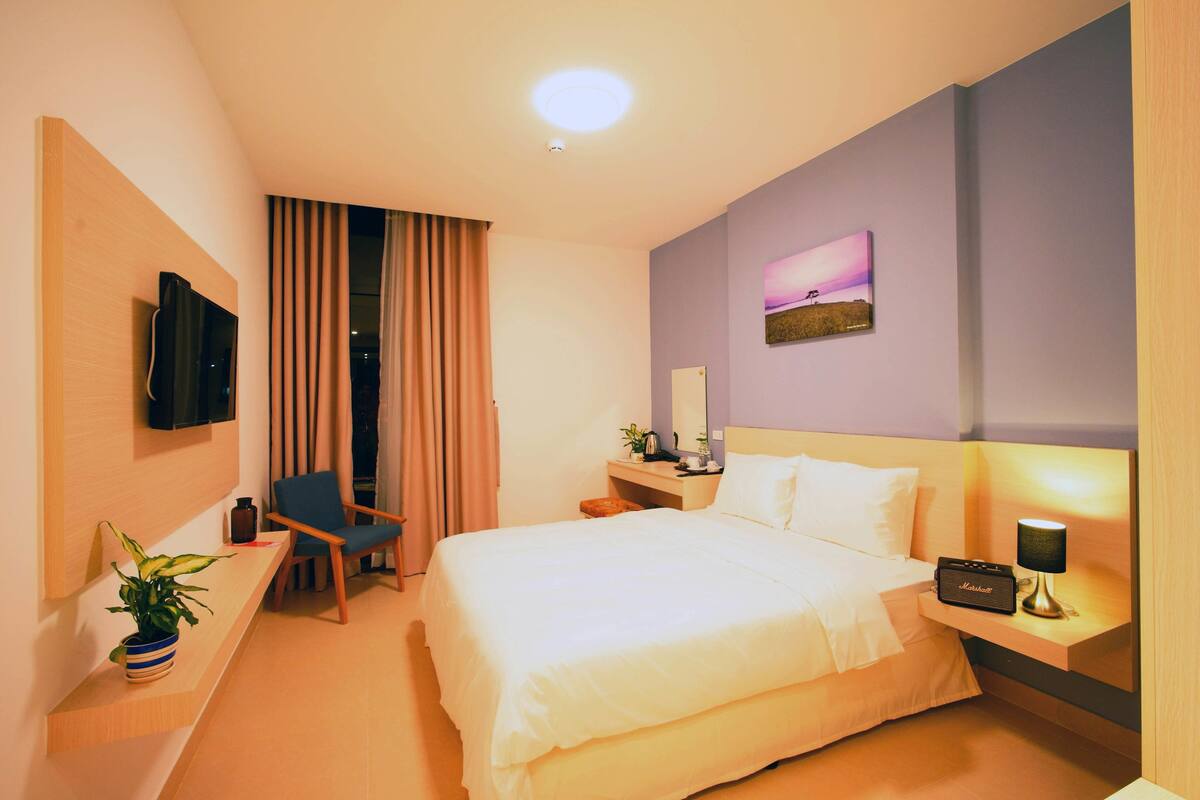 Ein Hotelzimmer mit Bett, Schreibtisch, Stuhl, Fernseher, Lampe und einem Bild an der Wand.