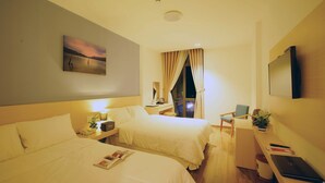 Habitación de hotel con dos camas, un escritorio con una computadora portátil, un televisor y un cuadro en la pared.