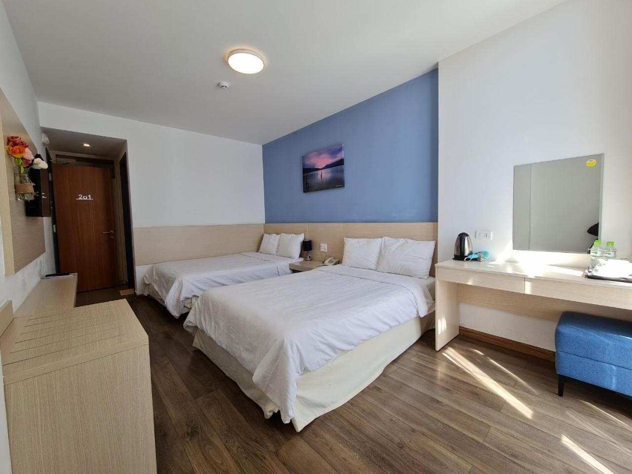 Habitación de hotel con dos camas, un escritorio, un espejo y un cuadro en la pared.