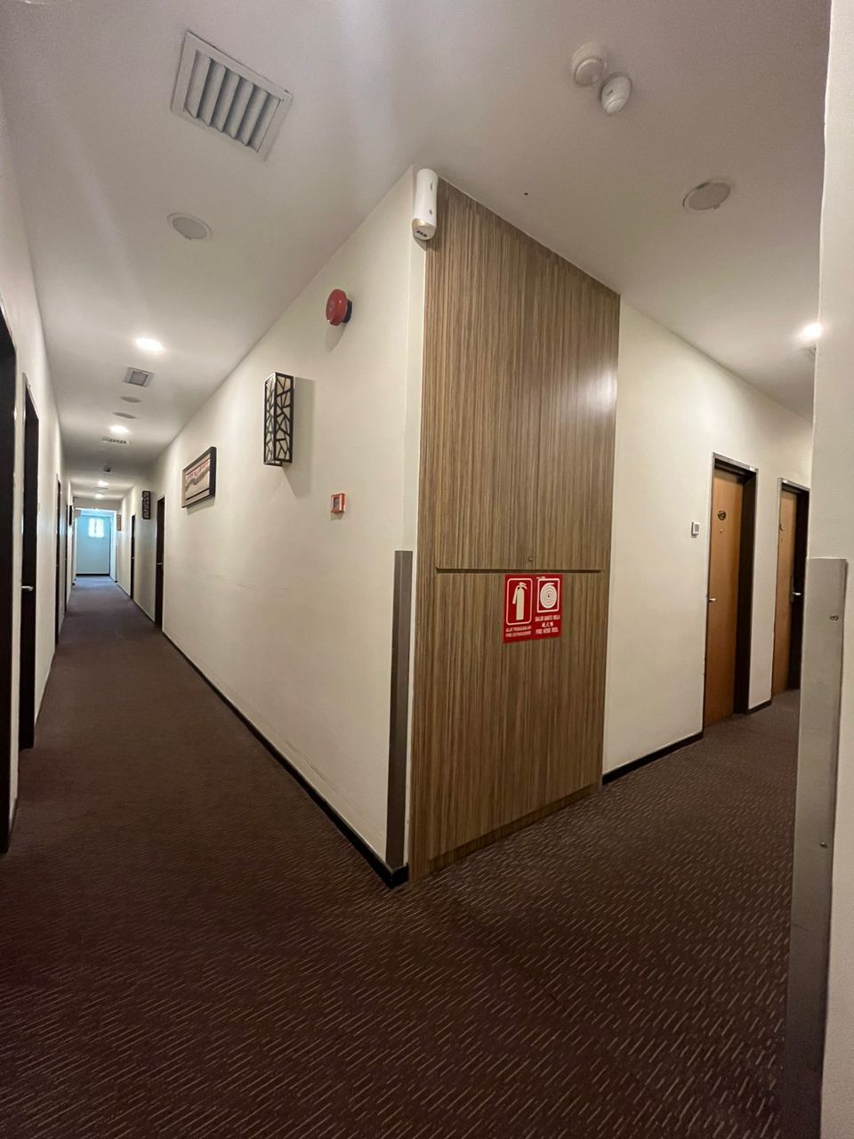 A hotel corridor with a wooden door, a fire alarm, and a sign indicating a fire exit.