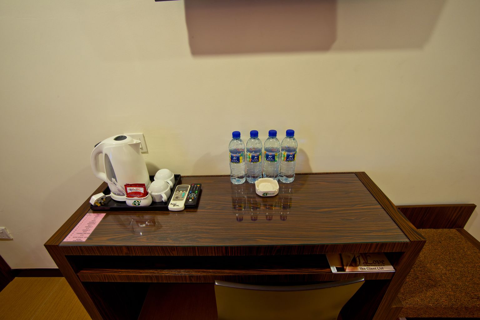 Een bureau in een hotelkamer met een koffiezetapparaat, afstandsbedieningen en flessen water.