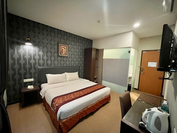 Una habitación de hotel con cama, mesita de noche, televisor y escritorio con silla.