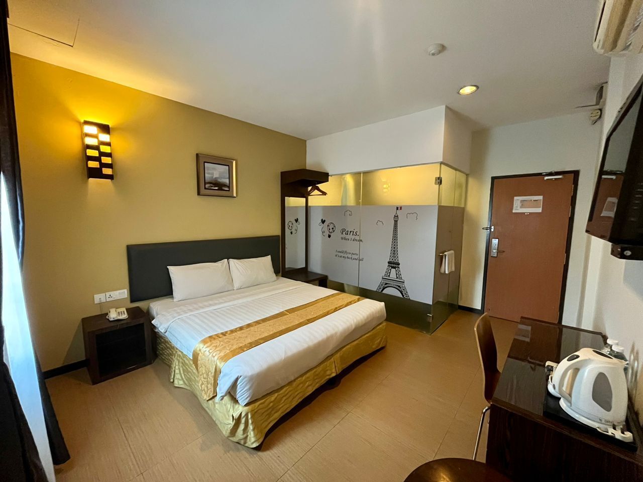 Ein Hotelzimmer mit Bett, Nachttisch, Lampe und einer Wand mit einem Bild und Text.