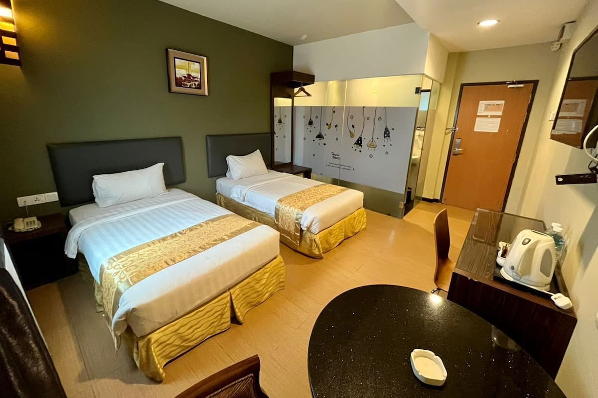 Une chambre d’hôtel avec deux lits, une petite table, une chaise, un bureau et un miroir.