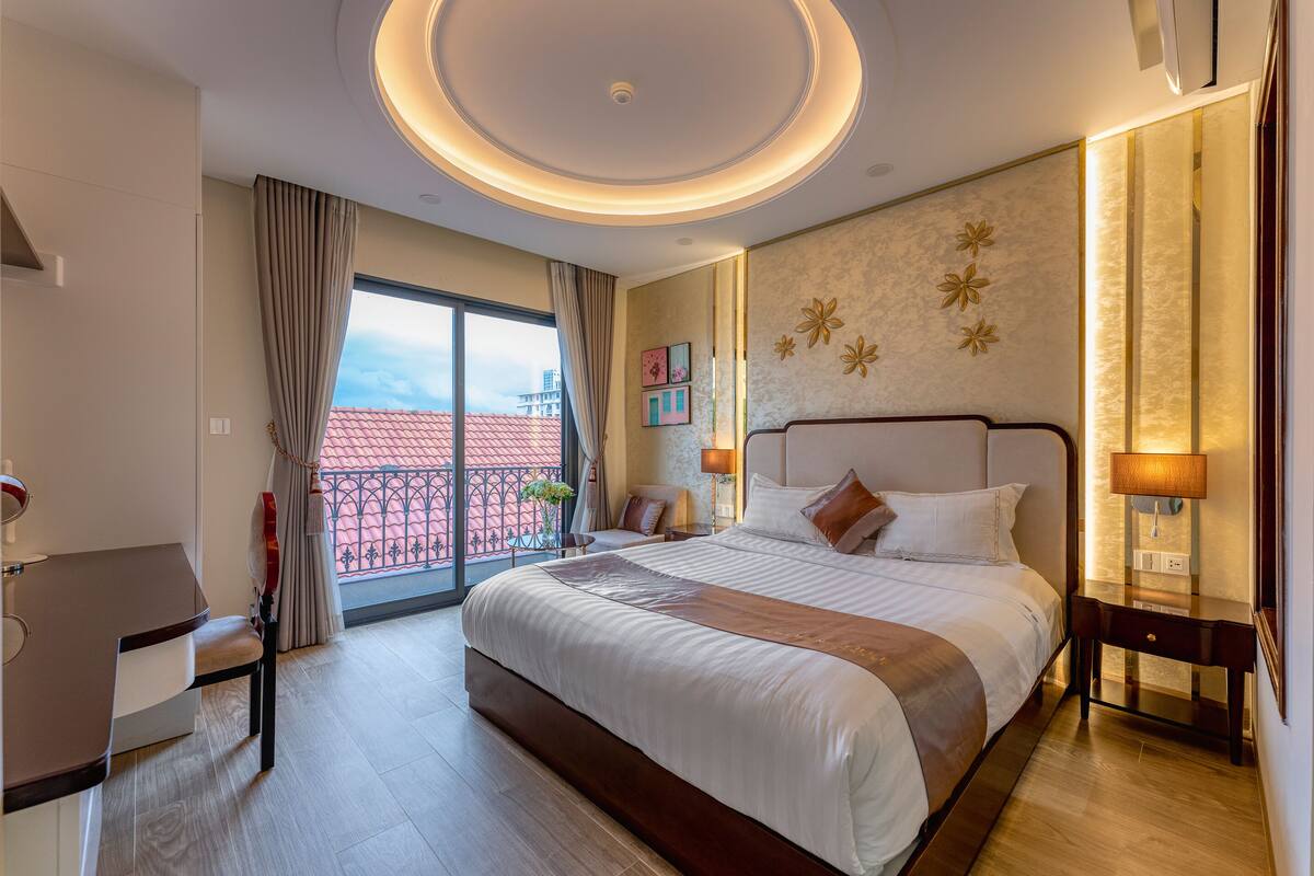 Hotelkamer met een groot bed, een bureau en uitzicht op een gebouw met rode daken.