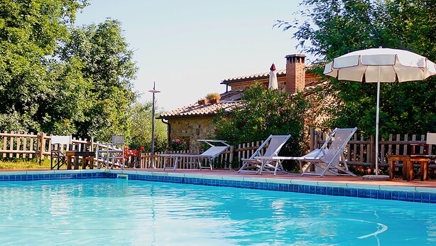 A swimming pool with lounge chairs and an umbrella, surrounded by a wooden fence and trees. - Casale Vigna Carbona (Gavorrano)