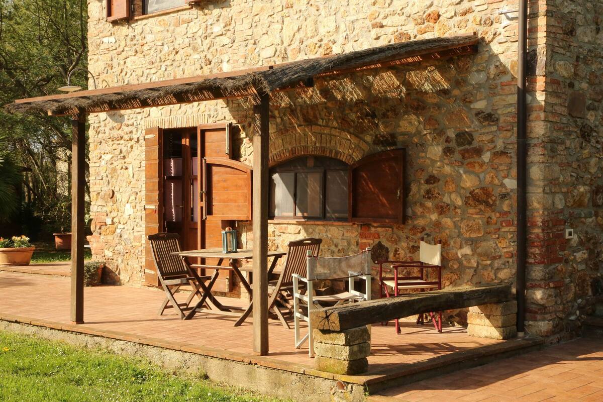 A stone building with a covered patio area featuring wooden furniture and a bench.