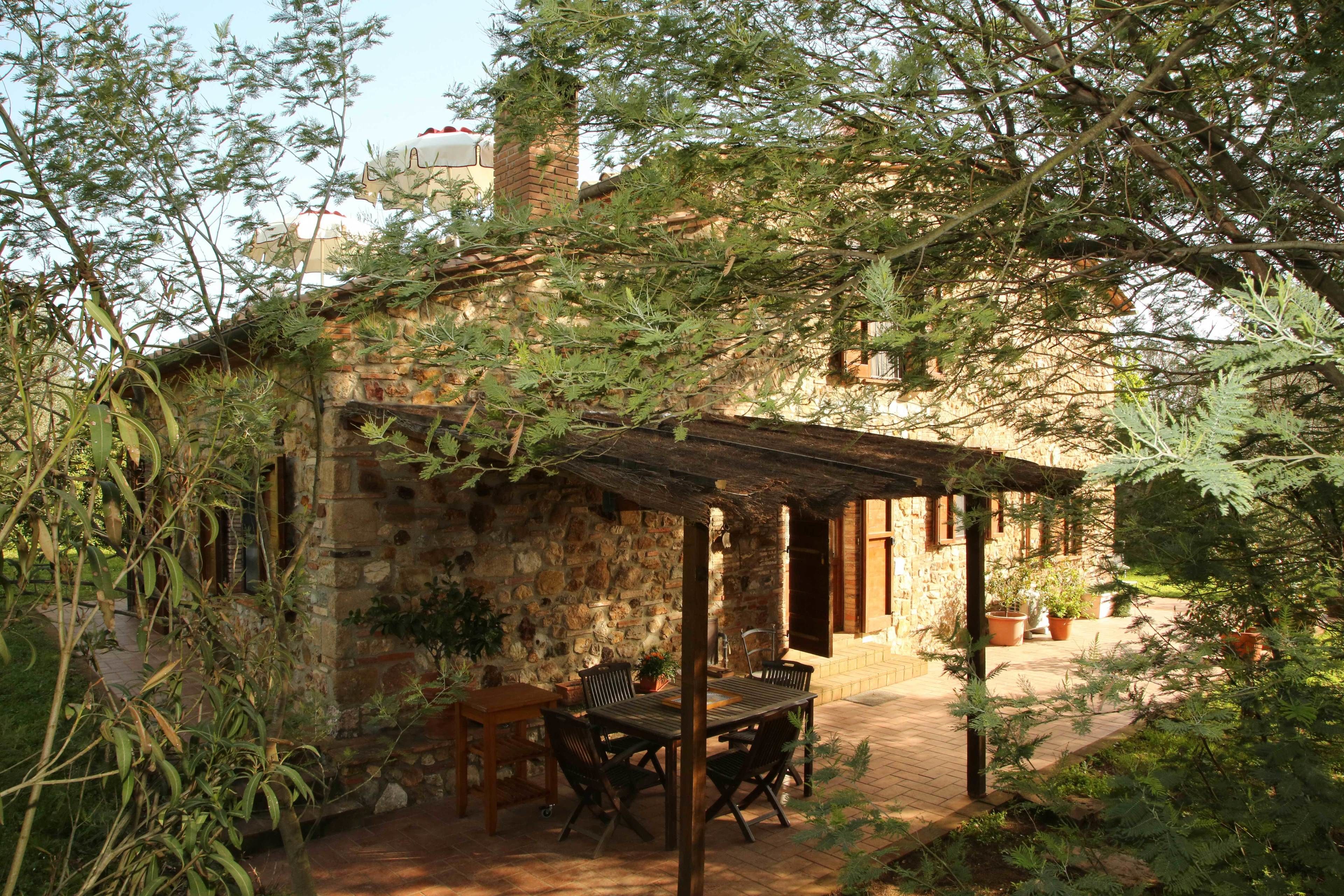 Ein rustikales Steinhaus mit einer Holzpergola, Sitzgelegenheiten im Freien und Topfpflanzen.
