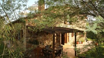 Ein rustikales Steinhaus mit einer Holzpergola, Sitzgelegenheiten im Freien und Topfpflanzen.