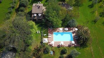 Eine Luftaufnahme eines Grundstücks mit Swimmingpool, Terrassenmöbeln und einem kleinen Gebäude mit Ziegeldach.