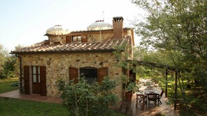 A stone house with a tiled roof, a chimney, and a small garden with a table and chairs. - Casale Vigna Carbona (Gavorrano)