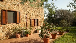 A stone building with multiple windows and potted plants in a garden area. - Casale Vigna Carbona (Gavorrano)