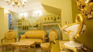Una habitación lujosa con muebles dorados ornamentados, un espejo grande que refleja un paisaje urbano y una araña.