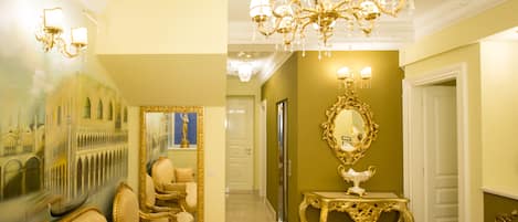 A luxurious hallway with ornate gold furniture, a large mirror, and a chandelier.