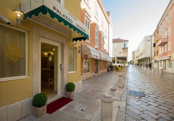 A street with a building labeled "PAZZO VENEZIA" with a red carpet and potted plants at the entrance. - Palazzo Venezia (Zadar)