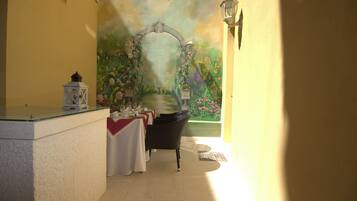 A narrow hallway with a dining area featuring a table set for a meal, a black wicker chair, and a decorative wall mural.