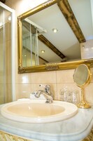 Un baño con un lavamanos de mármol, un espejo con marco dorado y un espejo redondo pequeño.