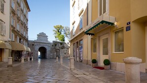 Una calle adoquinada con un arco histórico, un edificio amarillo con un letrero que dice "Palazzo Venezia" y una puerta con el número 4.