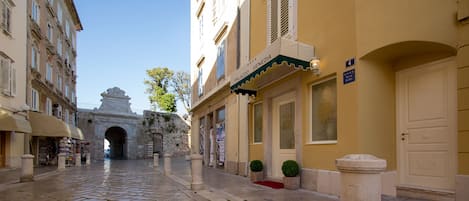 A cobblestone street with a historic archway, a yellow building with a sign reading "Palazzo Venezia," and a door marked with the number 4.