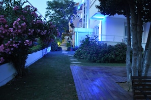 A pathway lined with lush greenery and flowering bushes, leading to a building with illuminated blue lights. - Dragos Island Hotel (Istanbul)