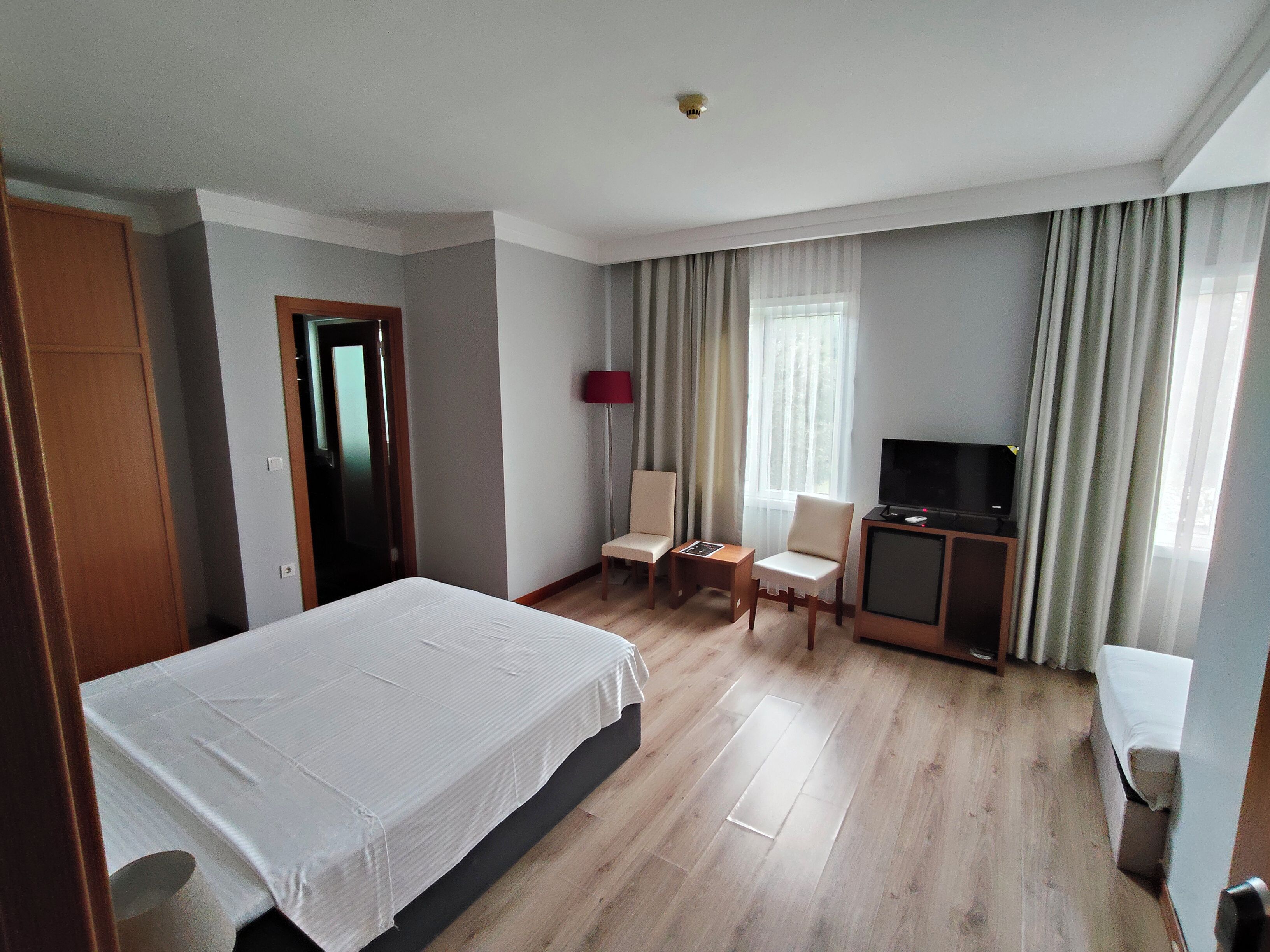 Habitación de hotel con cama, escritorio, silla, televisión y ventana con cortinas.