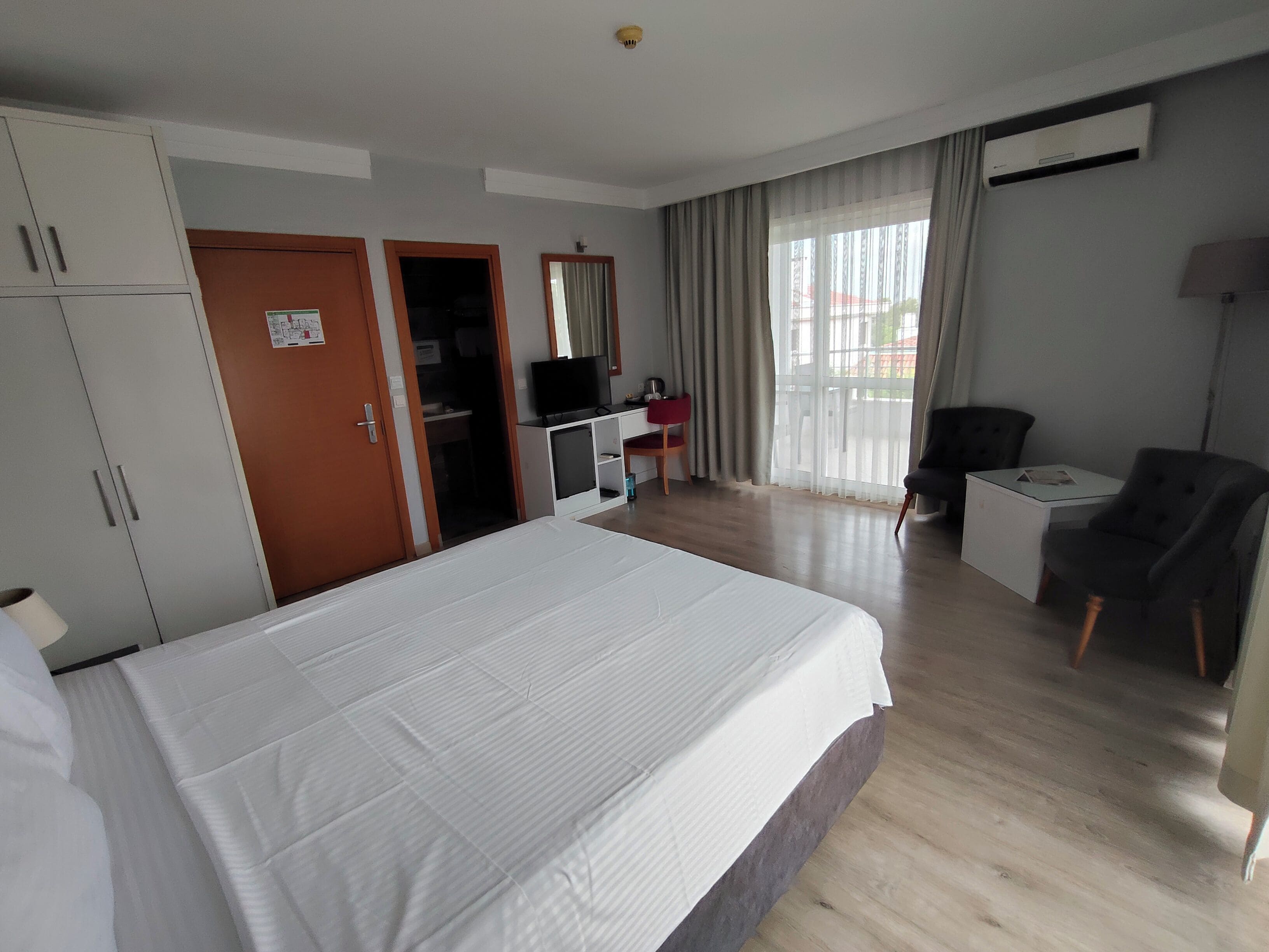 Una habitación de hotel con una cama grande, un escritorio con silla, un televisor y un ventanal con cortinas.