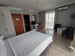 A hotel room with a large bed, a desk with a chair, a TV, and a window with curtains.