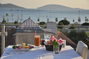 A table set with a meal, a drink, and a vase of flowers, overlooking a body of water and distant hills. - Dragos Island Hotel (Istanbul)