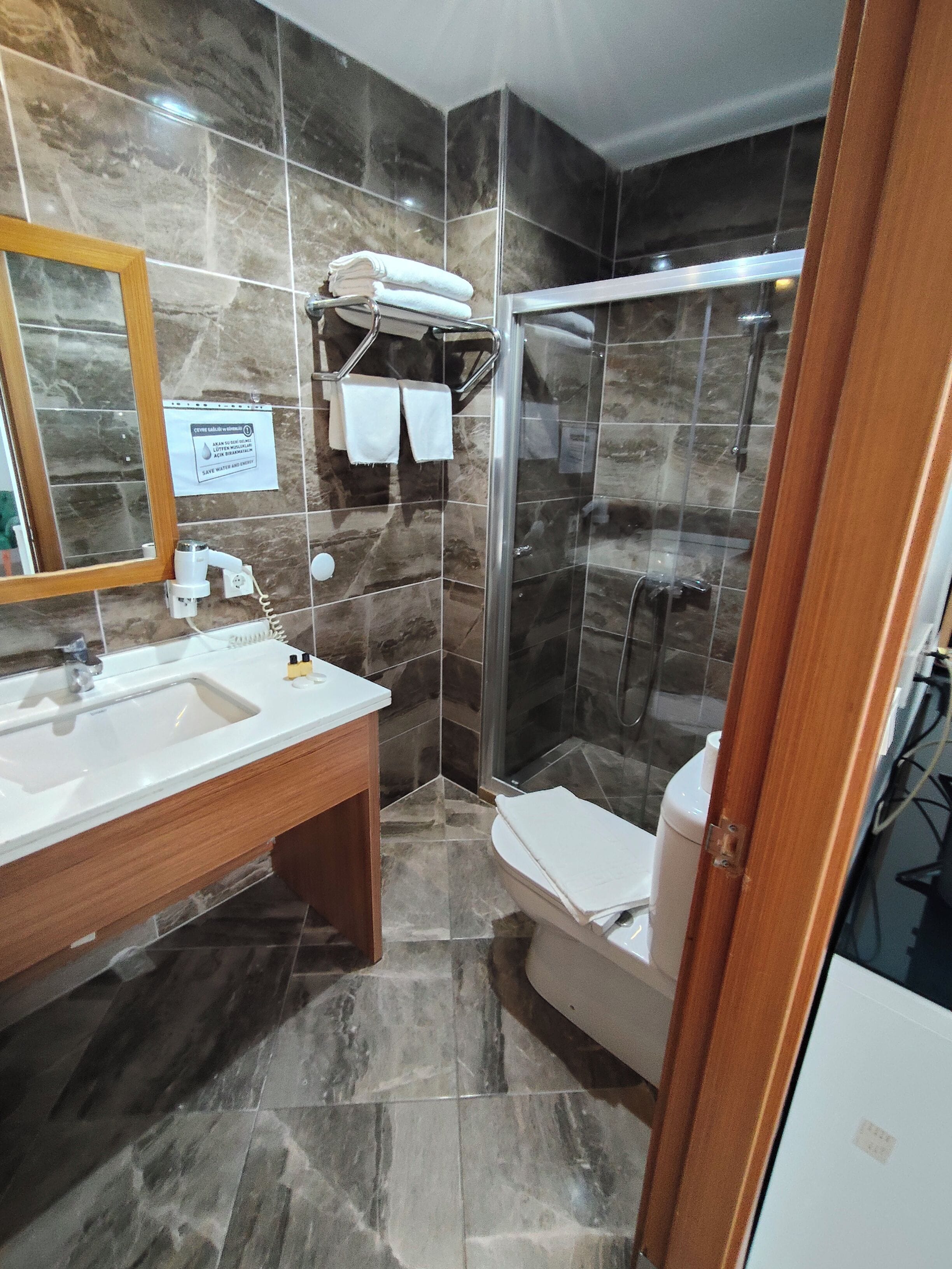 Un baño con piso de baldosas de mármol, un lavamanos con espejo, inodoro y cabina de ducha con mampara de vidrio.