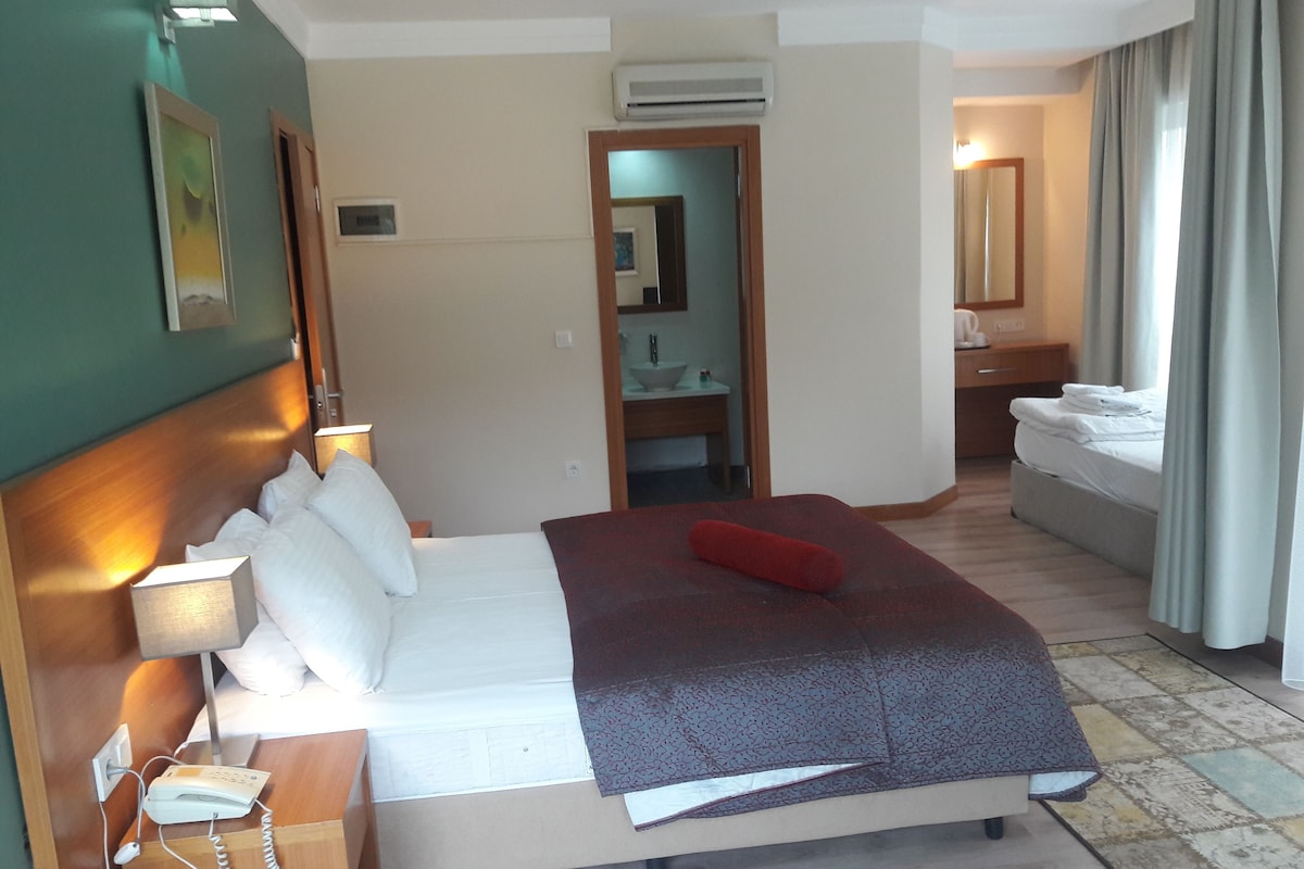 A hotel room with a bed, bedside lamp, phone, air conditioning unit, and a bathroom visible through an open door.