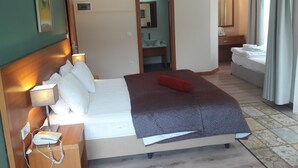 A hotel room with a bed, bedside table with a phone, a mirror, a bathroom visible through an open door, and a window with curtains. - Dragos Island Hotel (Istanbul)
