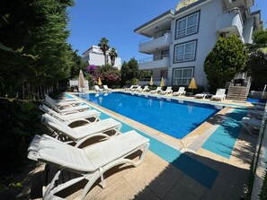 A swimming pool with lounge chairs and umbrellas, surrounded by greenery and a building with balconies. - Dragos Island Hotel (Istanbul)