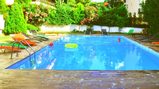 A rectangular swimming pool with a wooden deck, surrounded by lounge chairs and greenery. - Dragos Island Hotel (Istanbul)