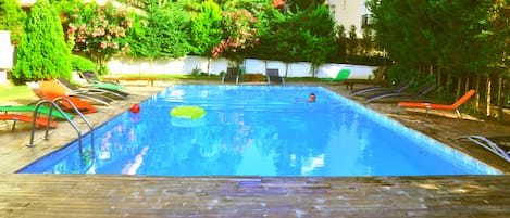 Una piscina al aire libre, sombrillas, sillones reclinables de piscina