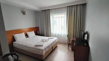 Ein Hotelzimmer mit Bett, Schreibtisch, Stuhl, Fernseher und einem Fenster mit Vorhängen.