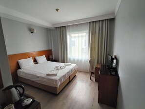 A hotel room with a bed, a desk, a chair, a television, and a window with curtains. - Dragos Island Hotel (Istanbul)