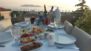 A table set for a meal with various dishes, drinks, and a scenic view of the sea and mountains in the background. - Dragos Island Hotel (Istanbul)
