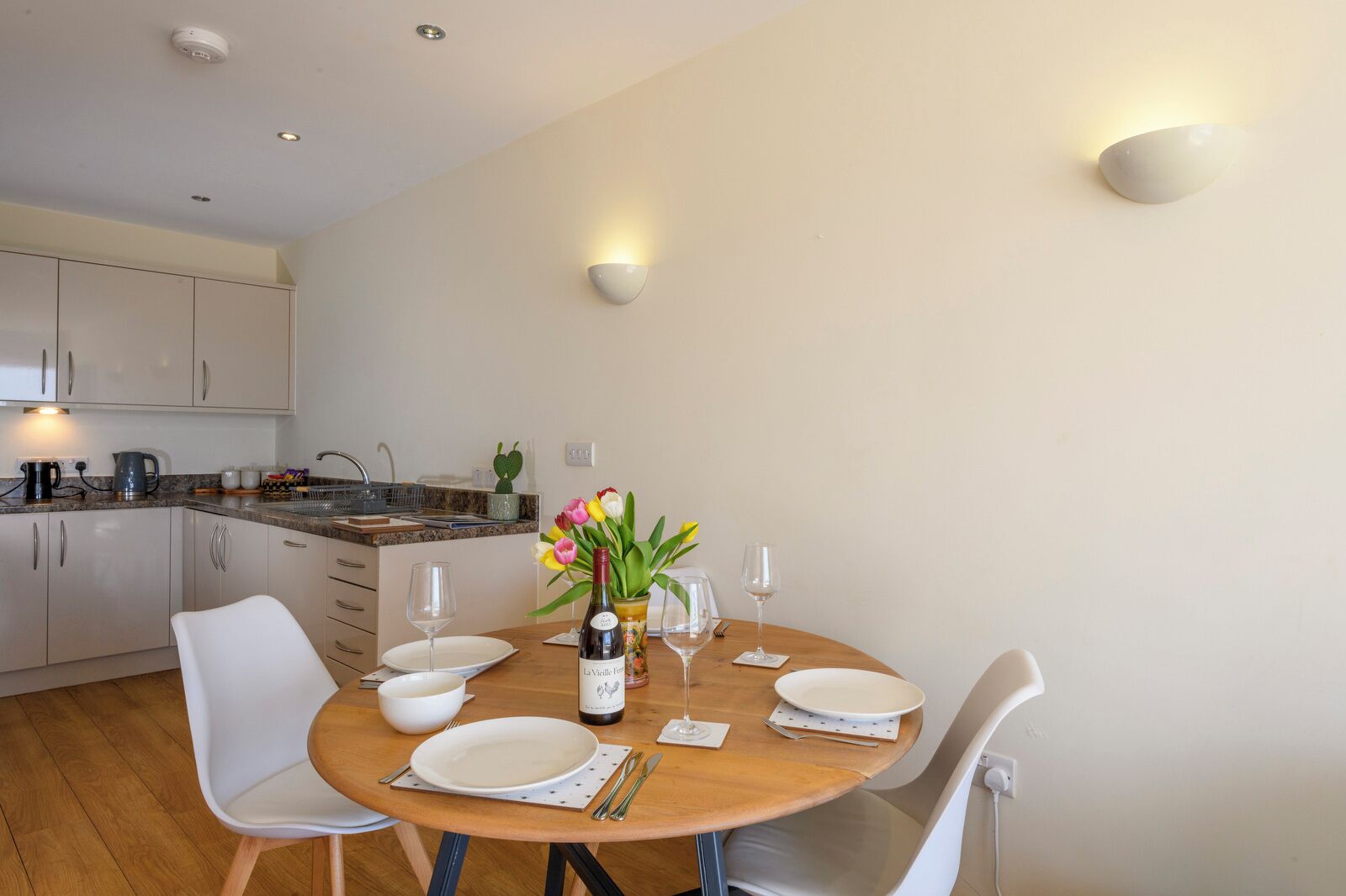 A modern kitchen with white cabinets, a granite countertop, and a dining area with a wooden table set for four.