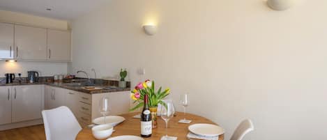 A modern kitchen with white cabinets, a granite countertop, and a dining area with a wooden table set for four.