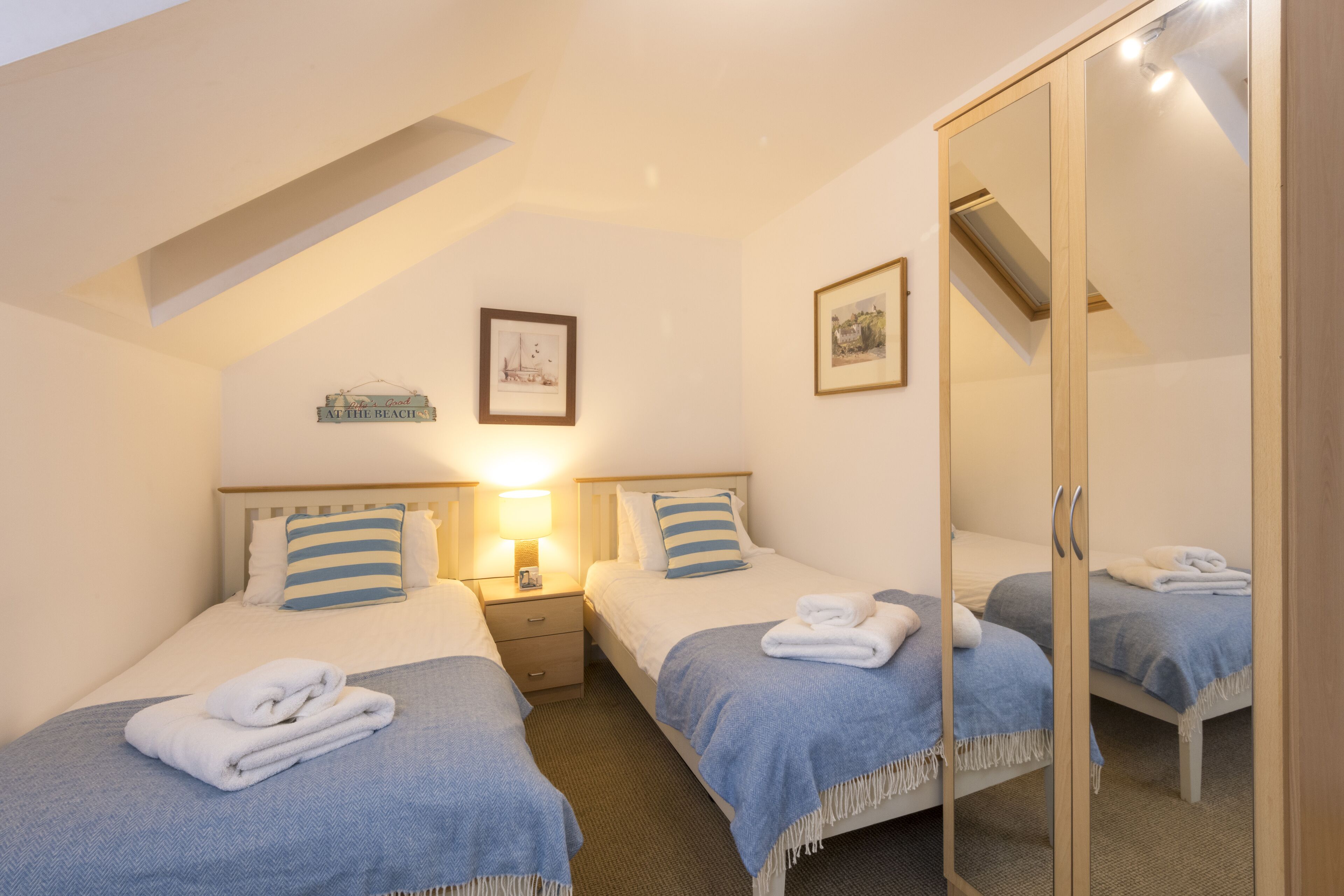 A bedroom with two beds, a mirror, and a small bedside table with a lamp.