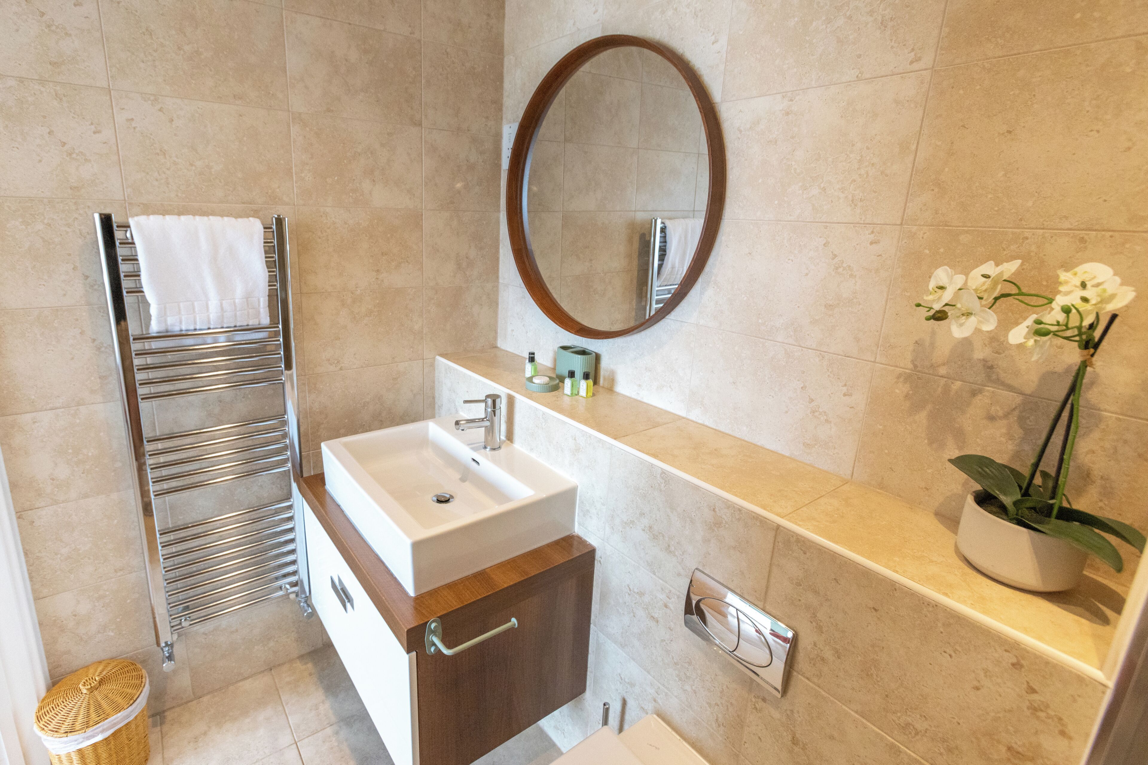 A bathroom with a white sink, a towel rack, a mirror, a potted orchid, and a wicker basket.