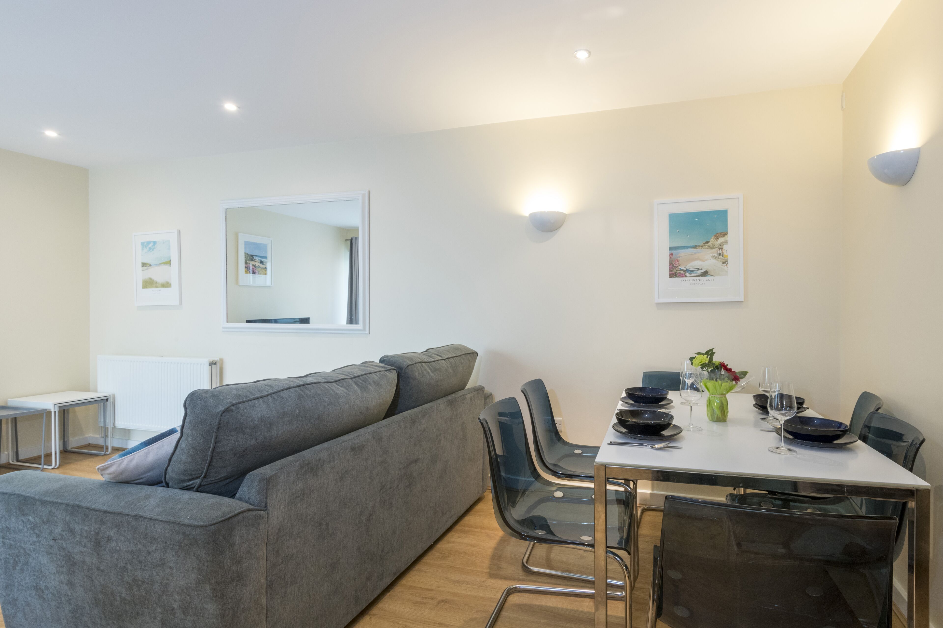 A modern living room with a grey sofa, a dining table with chairs, and a white radiator.