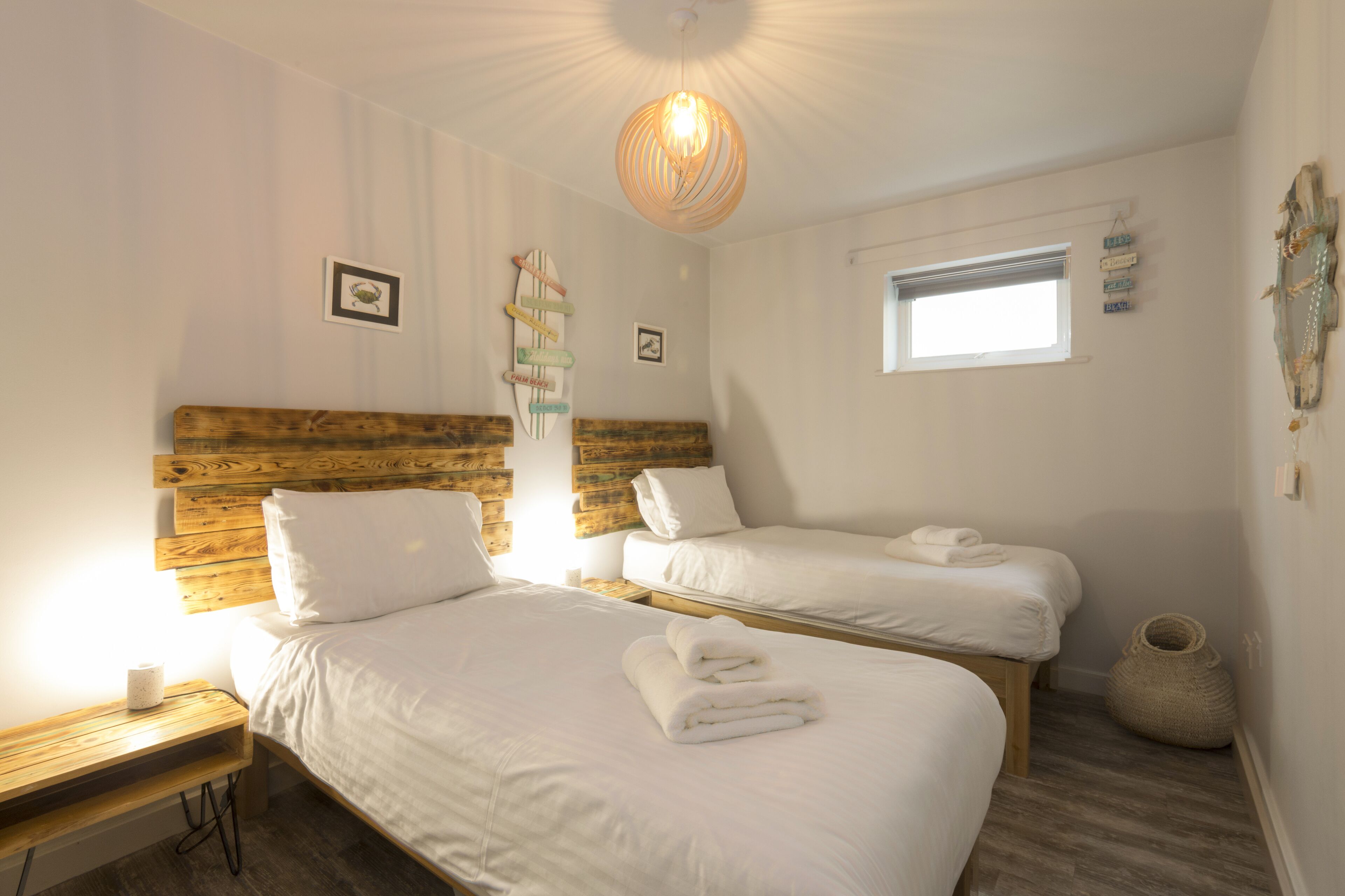 A bedroom with two beds, a wooden headboard, a hanging light fixture, a small window, and a wall-mounted decoration.
